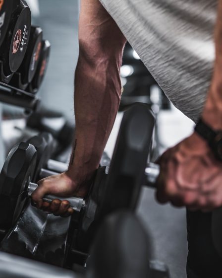 person in gray shirt holding black dumbbell