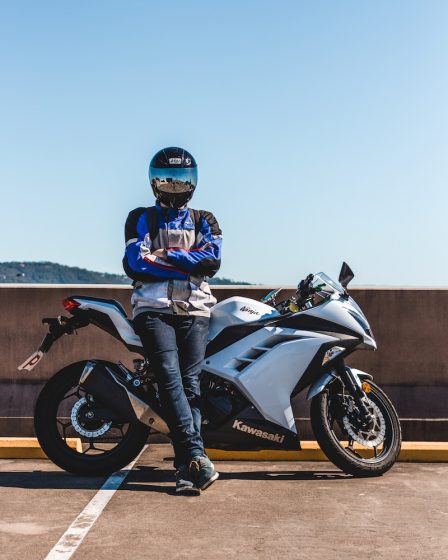 person wearing helmet standing and leaning on Kawasaki sports bike during daytime